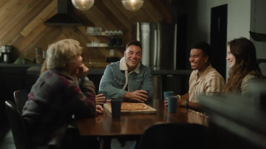 A group of friends laugh while drinking and eating pizza