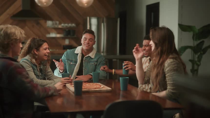 A small group of people are sitting at a table in a restaurant as they laugh and talk over a pizza