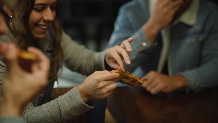 A girl picks pepperoni off her pizza and gives it to her friend