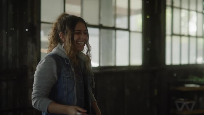 A young woman is smiling and laughing as she plays table tennis and looks at the paddle in her hand