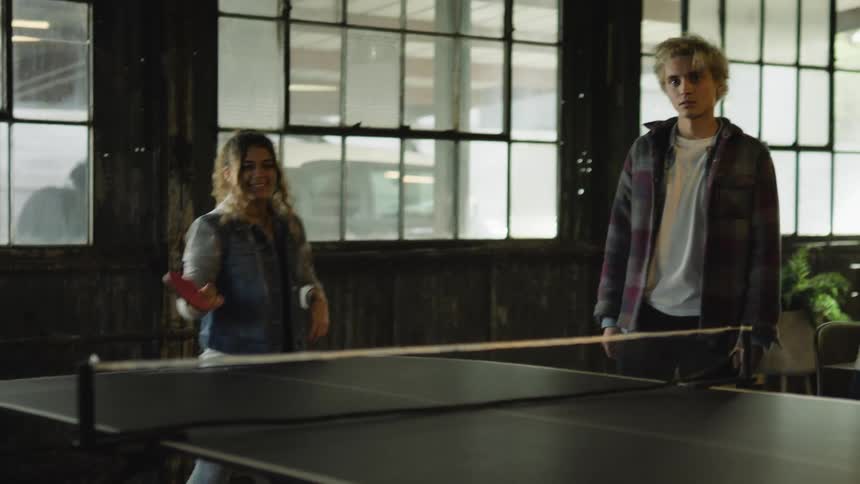 Two teenage boys watch as a teenage girl plays ping pong
