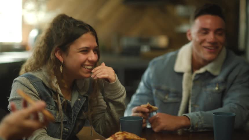 A group of friends laughing out eats pizza and drinks from cups