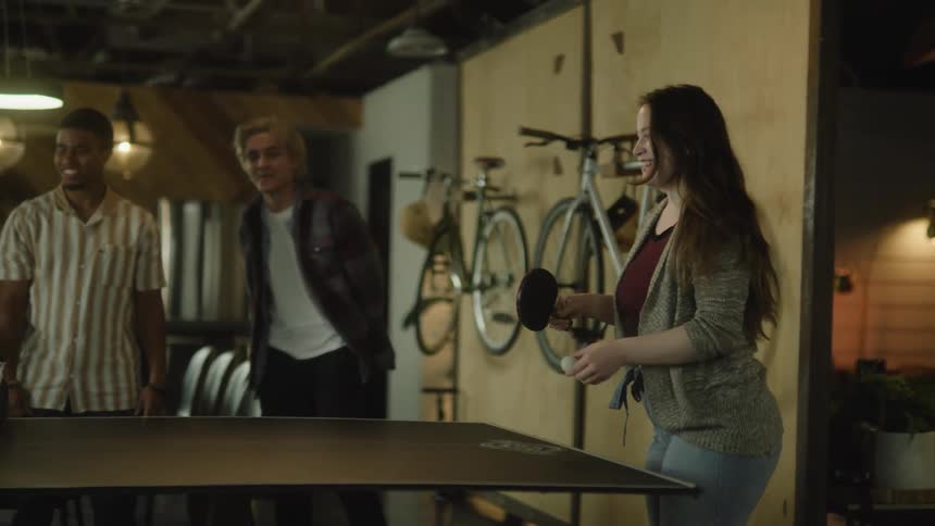 Teenagers laugh while playing ping pong in a shop