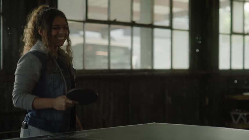 A female is laughing while playing ping pong indoors