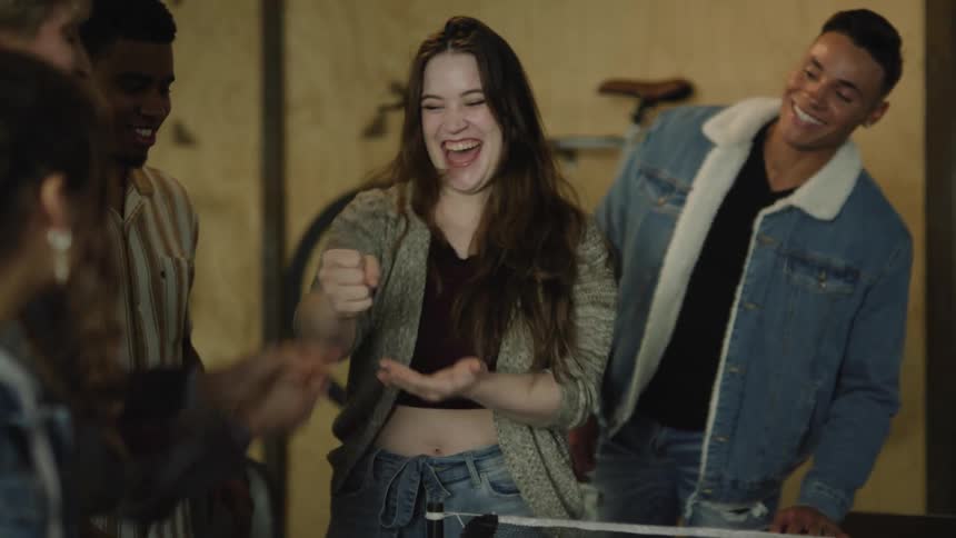 Four teenagers laugh as a boy and girl play rock paper scissors and then a boy holds up the girls arm when she wins