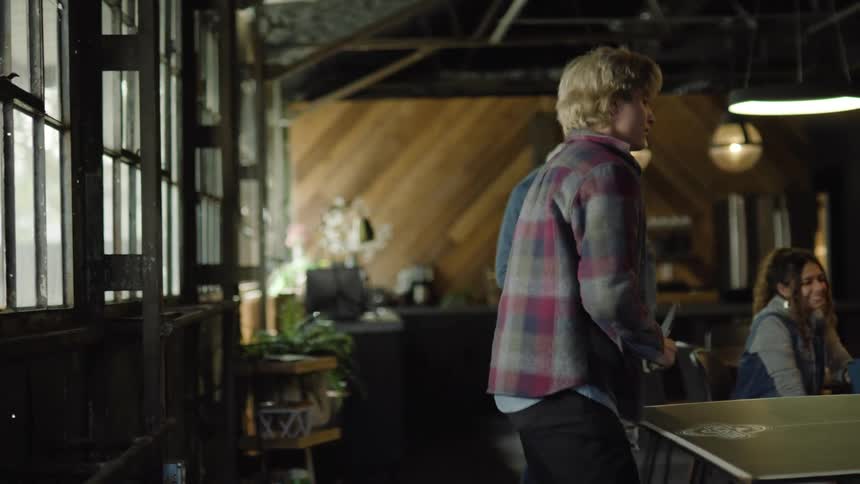A teenage boy plays ping pong as his friends watch