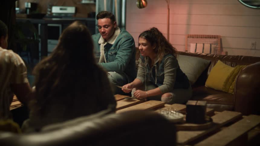 Friends sitting on brown couch play cards and laugh in room
