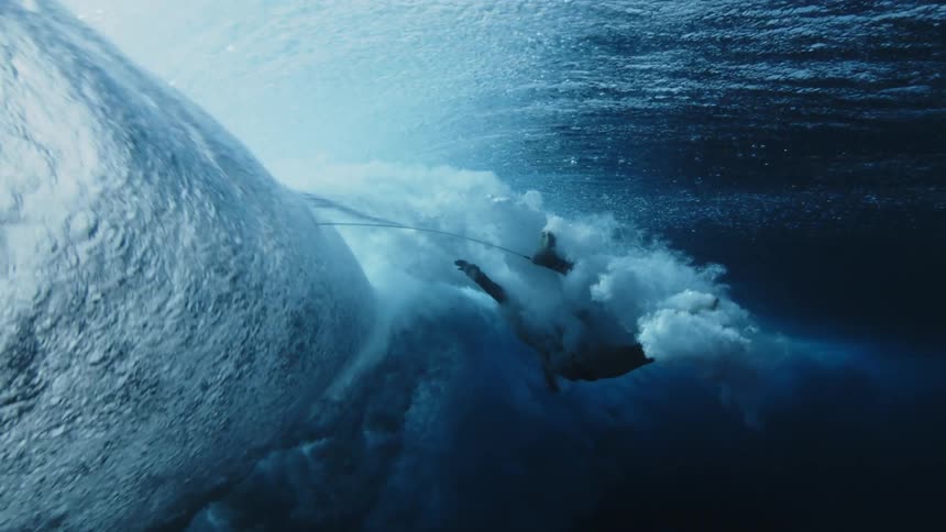 Underwater view looking up as a wave rolls overhead and a swimmer is in the water