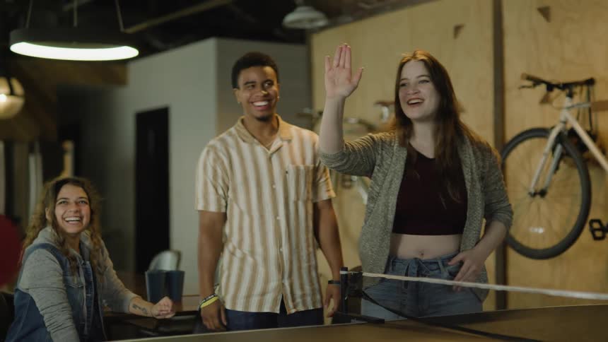 A man high fives his friends while playing ping pong