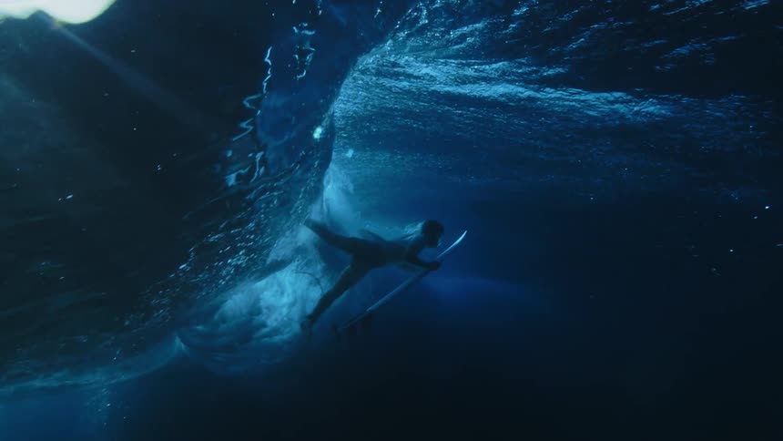 Underwater view of a surfer who went under riding a wave and he holds his surfboard and swims back up to the surface