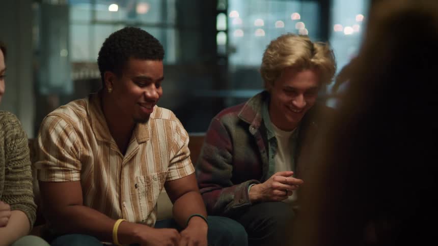 A group of friends sitting on couches talks to each other and laughs out in the living room
