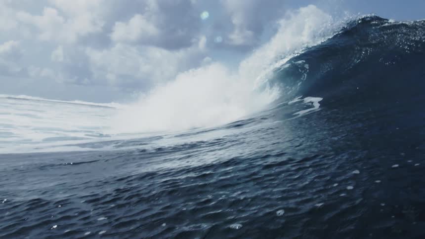 A large wave crashes in the ocean during the day