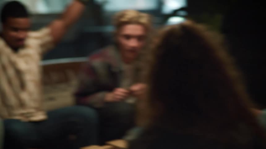 A small group of people are sitting around table laughing and a woman high fives one of the guys
