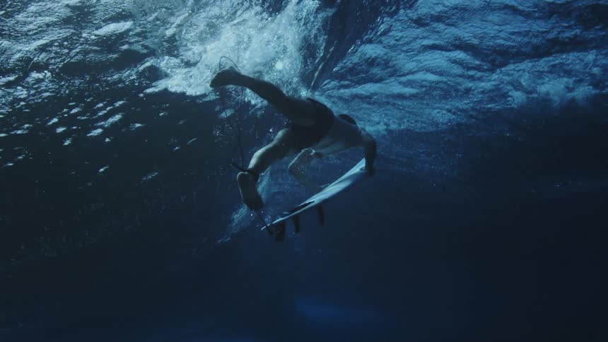 A male surfer holds his surfboard while swimming underneath a wave