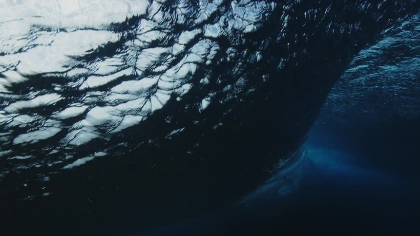 Underwater view of the seabed and looking up as a wave rolls overhead and sunlight reflects on the ripples on the surface