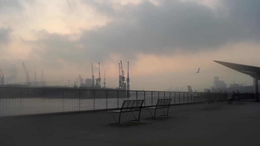 Two benches and a fence facing a large harbor on a misty day