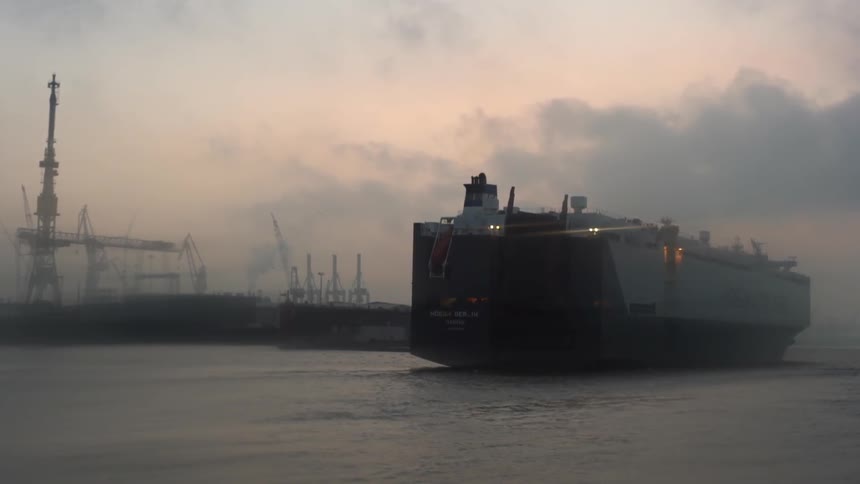 A ship sails from a harbor on a foggy evening