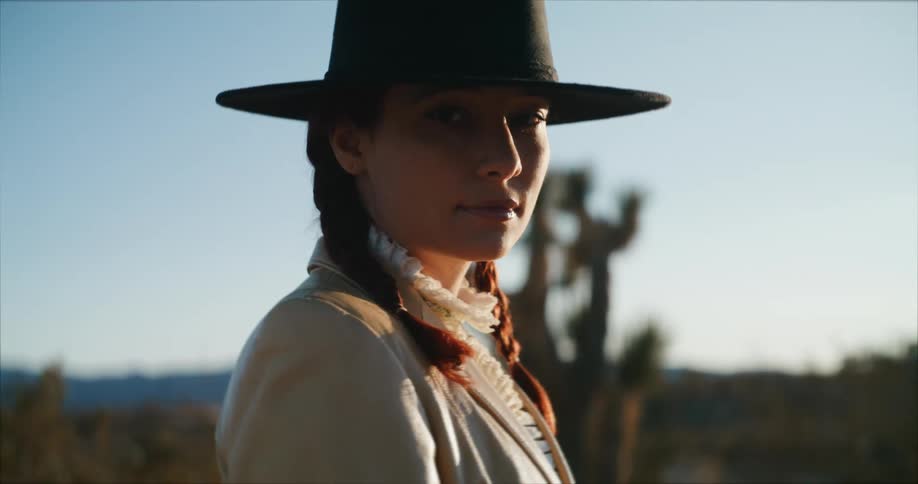 A woman wearing a black hat is standing outside in the desert under a clear sky