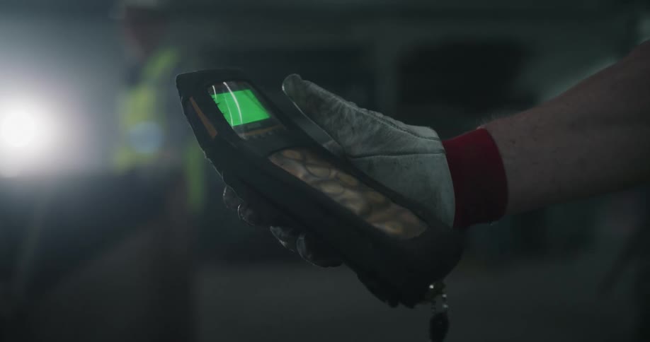 A man wearing a glove is holding an electronic device with a small green screen