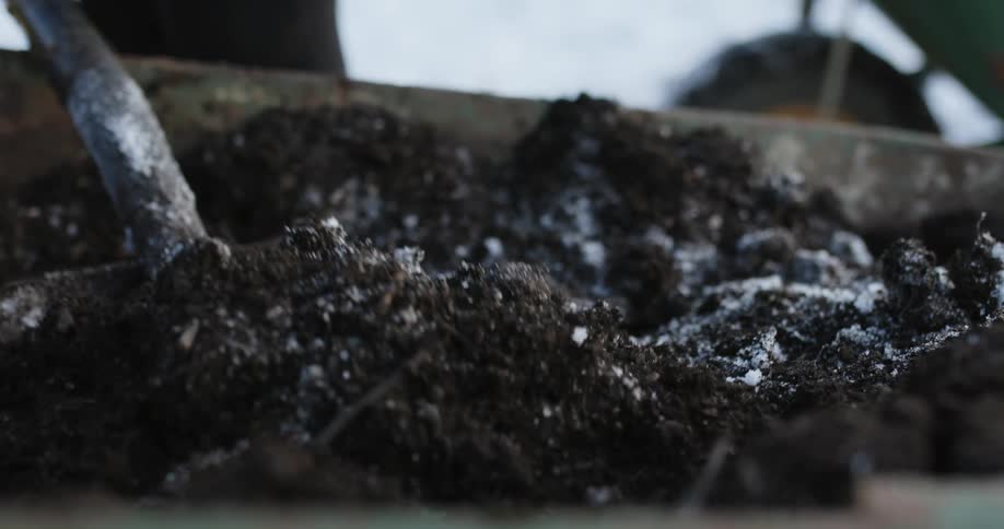 A person with a shovel is moving soil from a wheelbarrow