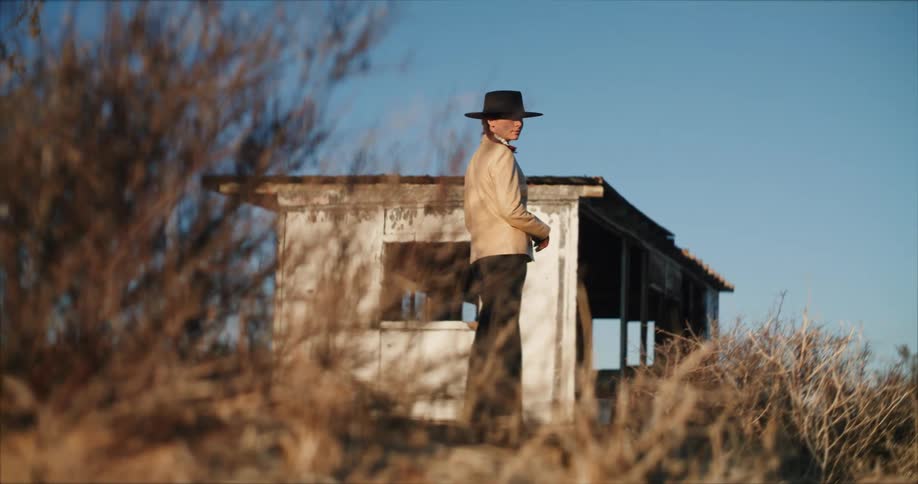 Woman wearing sunhat stands with house ruin in the background