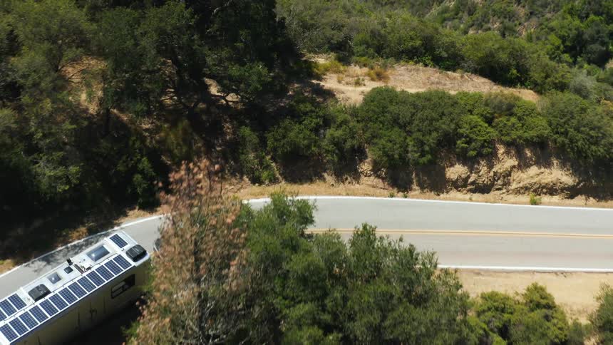 A truck pulls a mobile home on a road around a curve with many trees on a mountain