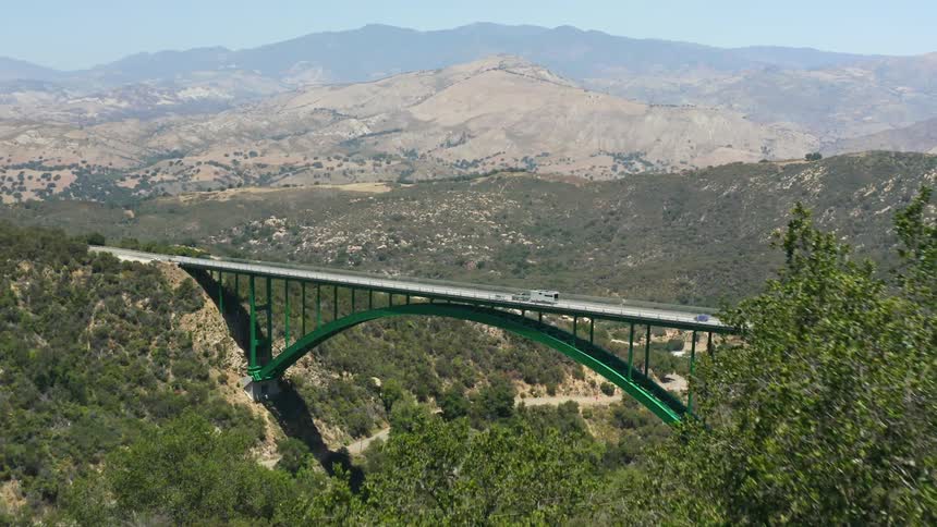 Traffic travels across a bridge between mountain ridges in the countryside during the day