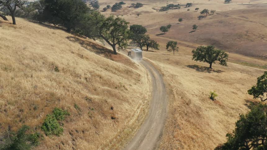 A truck pulls a mobile home on a hillside road around a curve with many trees