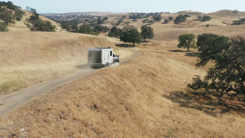 A truck hauls a trailer across a road in a rural area