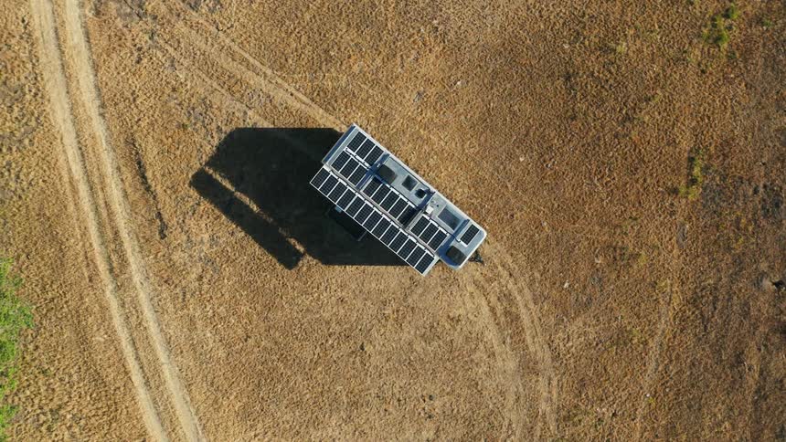 A mobile home with solar panels on the roof is parked off the road in a rural area