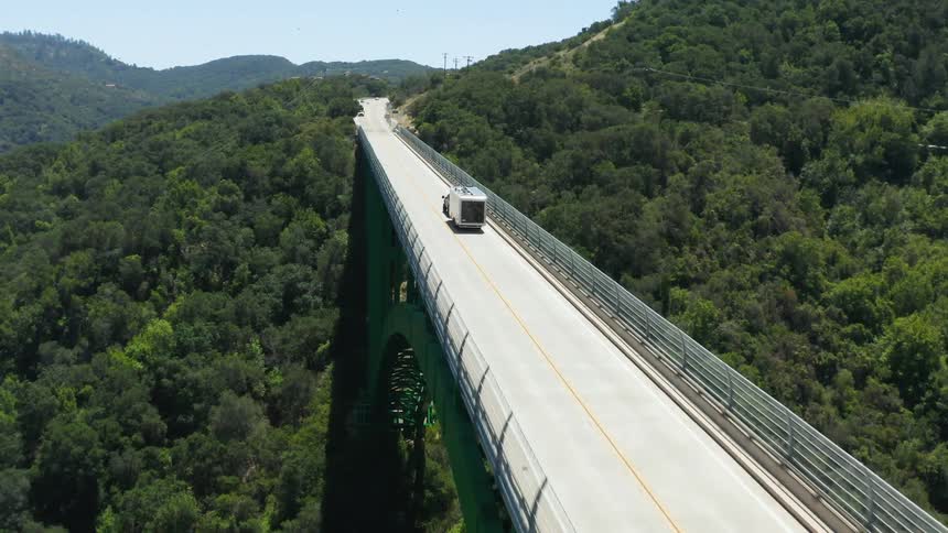 Vehicles drive across a bridge over a forest area