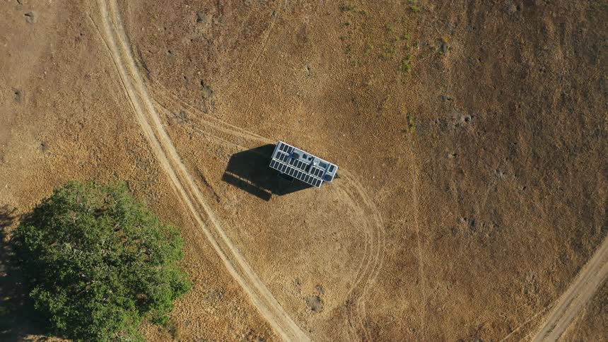 Top down aerial view of solar panels over a structure in the middle of a field in the countryside