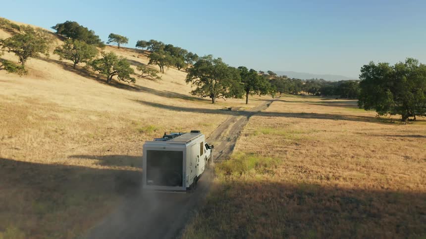 A truck pulls a large trailer along a dirt road through the countryside during the day