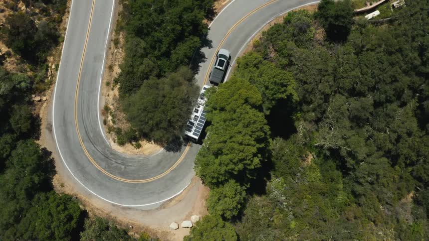 A truck travels along a winding road while towing a large trailer
