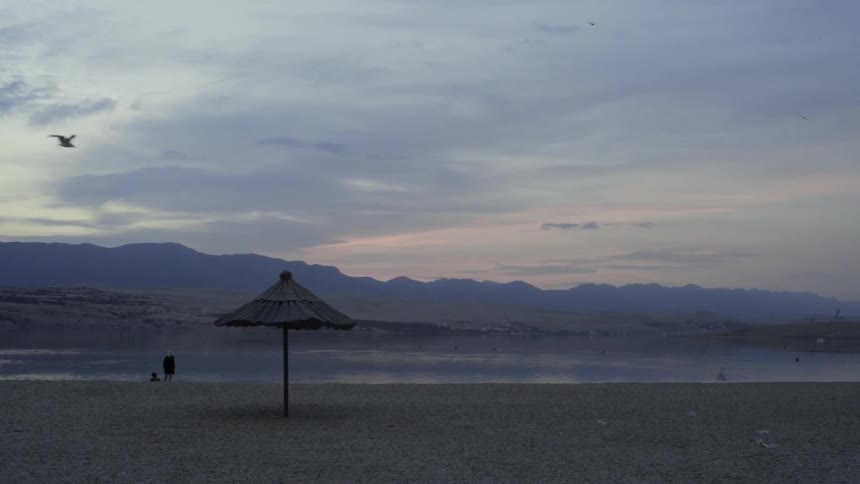 Someone standing next to a body of water near a mountain range on a cloudy evening