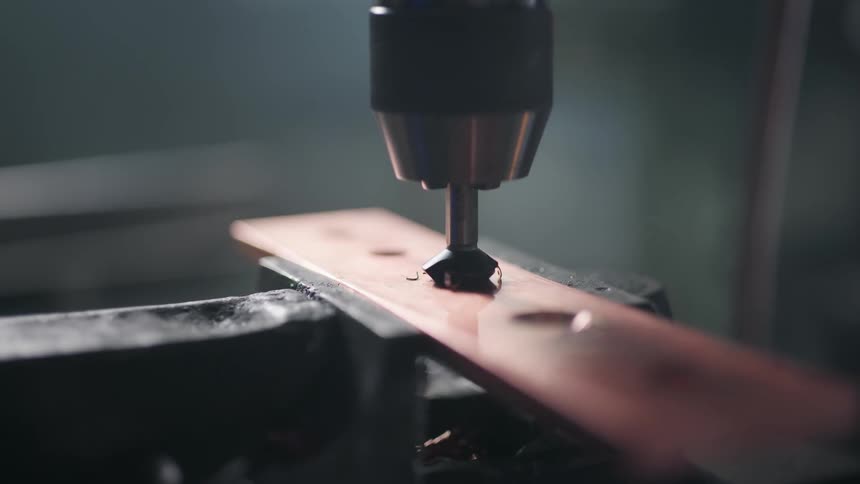 Drill is drilling into a piece of red metal that is in a vise