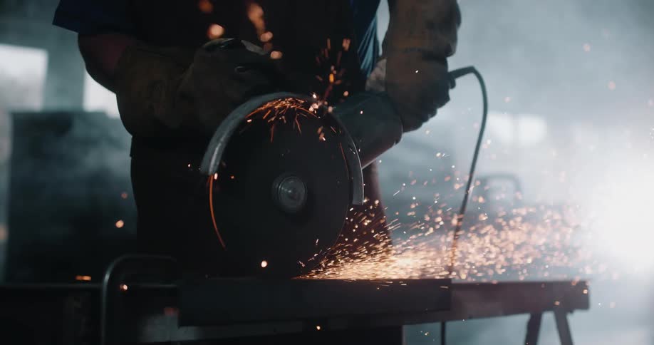Worker wearing protective gear uses metal power tool in workshop creating a shower of sparks