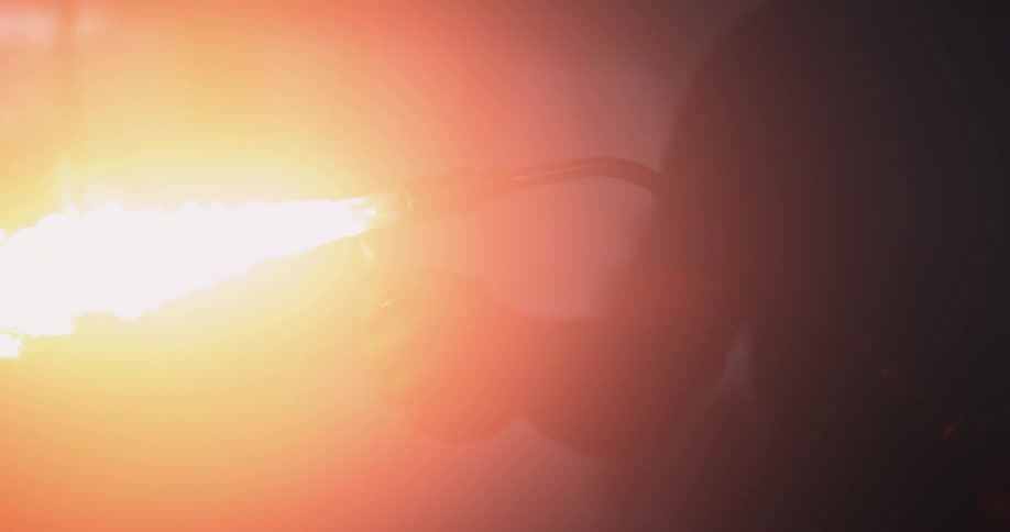 A man is holding a blowtorch as he lights a lighter and a bright flame shoots across the air