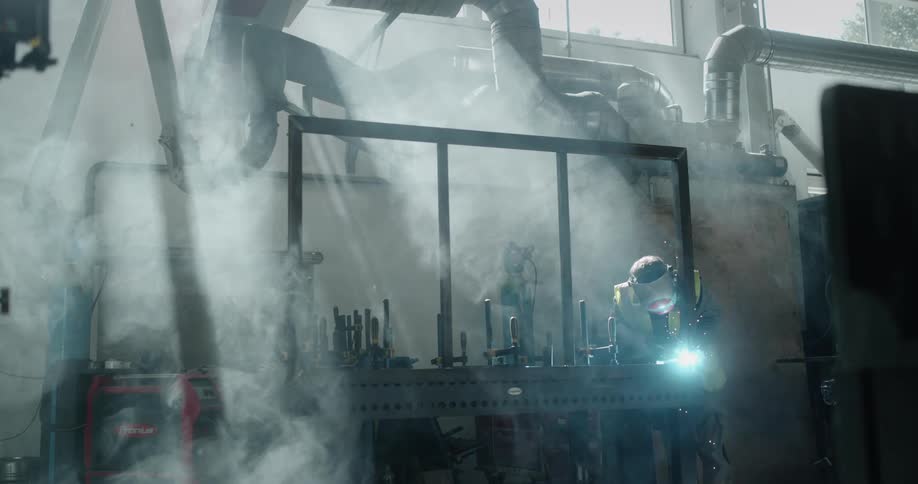 Light shines as welder works on joint in fog filled workshop