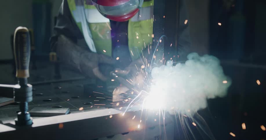 A man in a full protective outfit is welding metal in a workshop