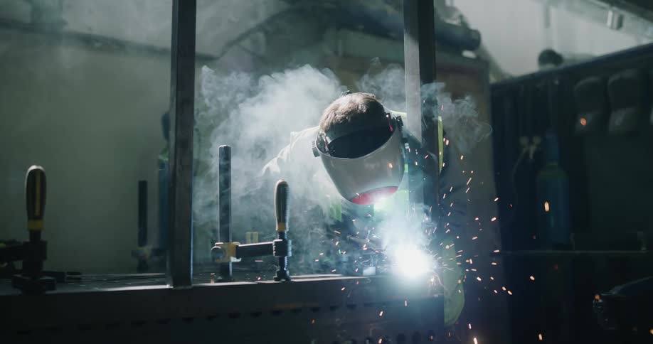 Sparks fly and welder creates bright light while welding parts together in workshop