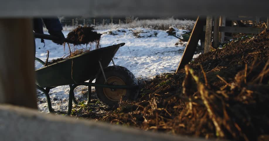 A person using a pitchfork to move dirt and hay