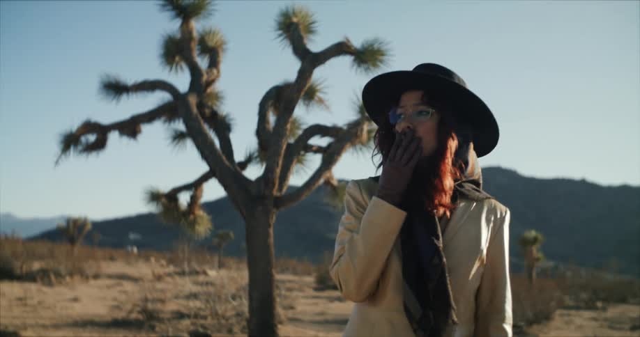Woman wearing a coat and hat smokes a cigarette in the desert at morning