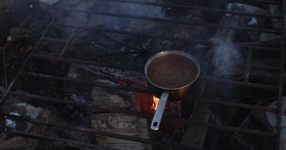 A frying pan is sitting outside on a grill with a flame burning as smoke rises