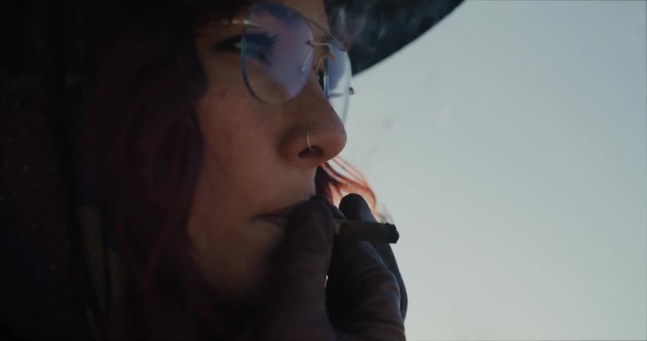 A woman is outside holding an open lighter as she lights a cigarette