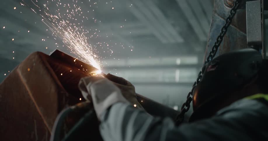 Sparks fly as a person wearing a welding helmet is welding metal