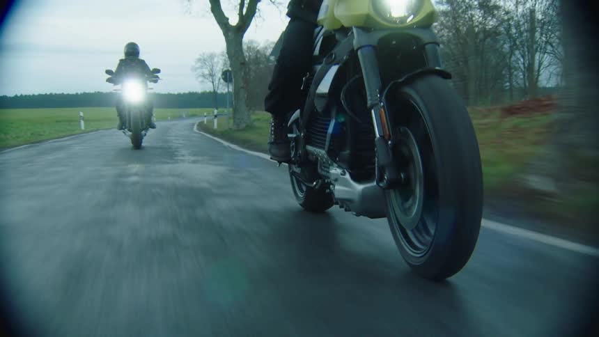 Two people dressed in all black are riding their motorcycles down the street
