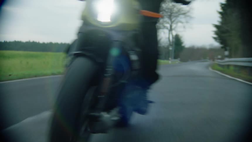 A cyclist is riding a motorcycle on a rural road with trees in the distance