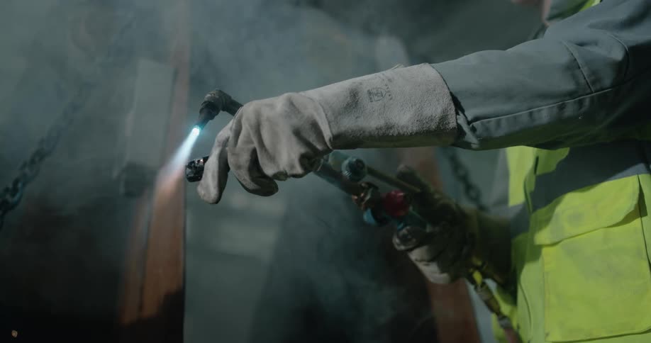 A man moves an item awat from a welding torch that is lit up