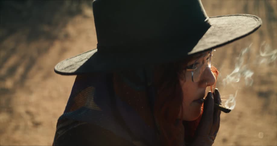 Young woman wearing a hat lights a cigarette and starts smoking outdoors
